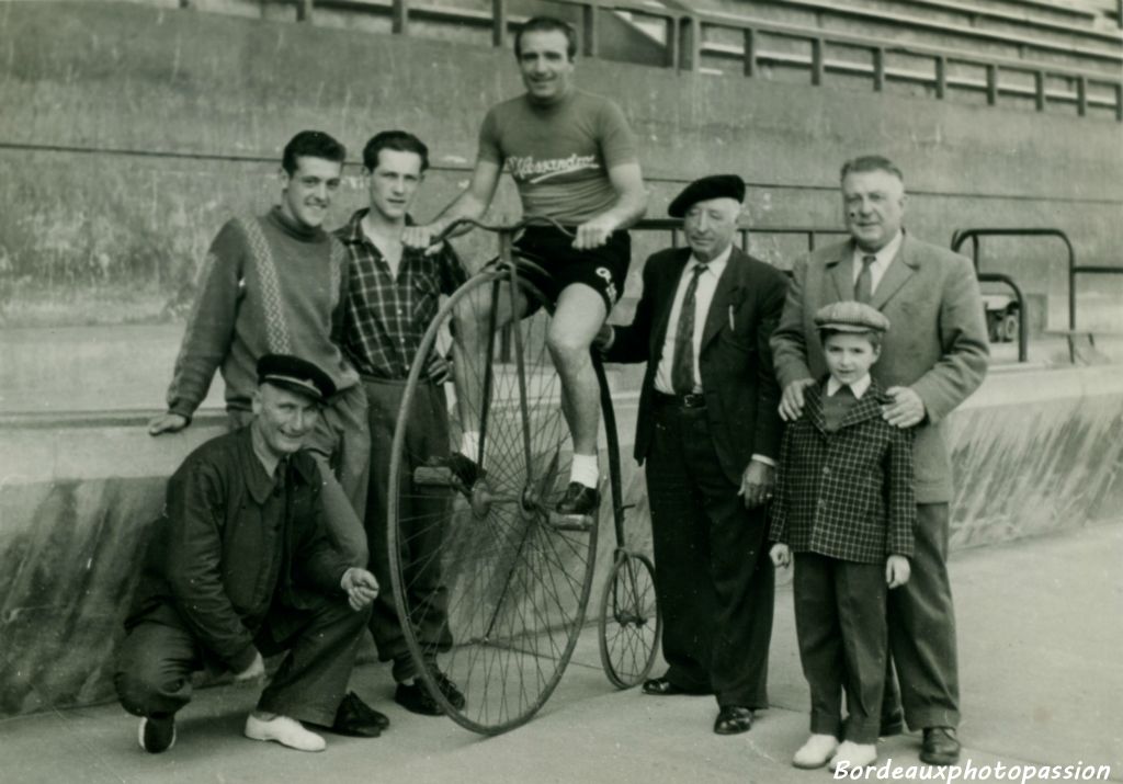 Marcel accroupi sourit de voir le champion cycliste Serge Lapébie sur un grand bi. À droite, le speaker des courses,  le directeur du stade  et le fils de Lapébie.